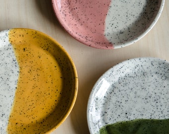 May include: Three ceramic plates with speckled white glaze and a contrasting colored half-circle design. The plates are pink and white, yellow and white, and green and white.