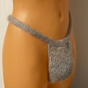 May include: A gray knitted pouch with a wide waistband. The pouch is made of a soft, fuzzy yarn.