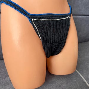 May include: Black knitted underwear with a blue trim and a decorative rhinestone border. The underwear is displayed on a mannequin. The garment has a string-style design.
