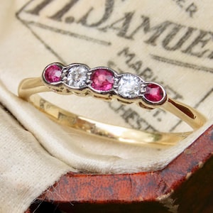 Peut inclure: Une bague en or avec un sertissage à cinq pierres alternant des rubis rouges et des diamants blancs transparents de taille ronde. Les pierres sont disposées en rangée horizontale, avec trois rubis et deux diamants sur une monture en or.