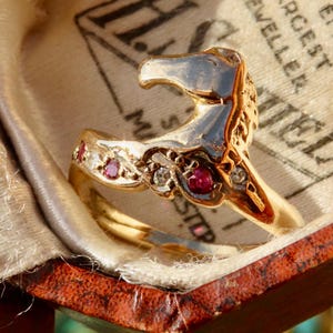 May include: A gold ring featuring a sculpted horse head design. The band is embellished with alternating small round red rubies and clear white diamonds set along the side. The metal has a polished finish, reflecting light across the surface.