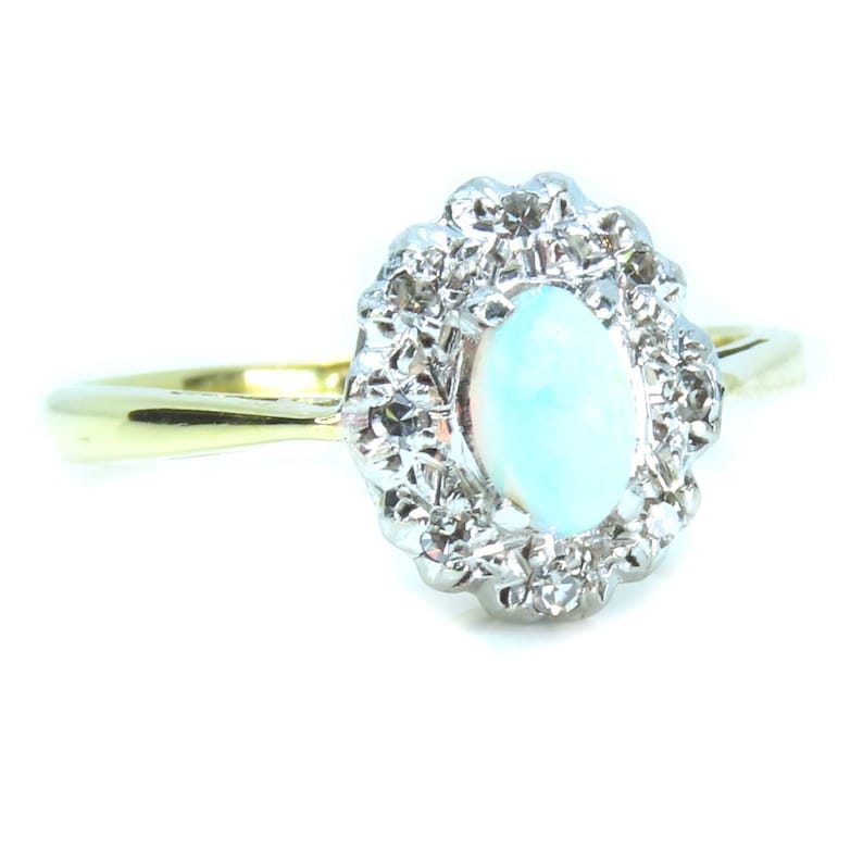 May include: A gold ring with a light blue oval gemstone at the center, surrounded by a halo of smaller, clear stones. The ring's band is a simple, polished gold.