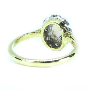 May include: A gold ring with an oval-shaped center stone, surrounded by smaller diamonds. The ring's band is a polished gold color, and the setting features a cluster of diamonds at the top. The ring is set against a white background.