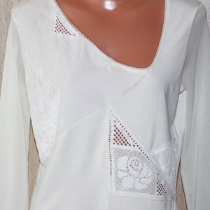 May include: White long-sleeved shirt with a lace overlay in a geometric pattern. The lace features a floral design.
