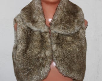 May include: A faux fur vest in shades of brown and tan. The vest has a wide collar and a button closure. The fur appears soft and plush, with a natural-looking texture. The vest is displayed on a mannequin.