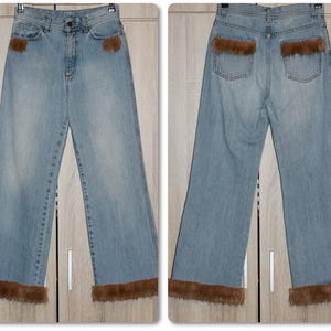 May include: A pair of light blue denim jeans with brown fur trim around the bottom of the legs. The jeans have a straight leg style and have a zipper fly.