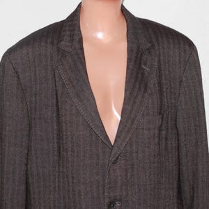 May include: A dark brown blazer with a herringbone pattern. The blazer has a single-breasted closure with three buttons and a pocket on the left side.