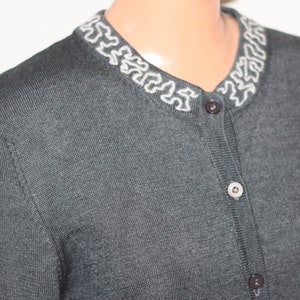 May include: A dark gray cardigan with a white embroidered trim around the neckline. The cardigan has a button closure.