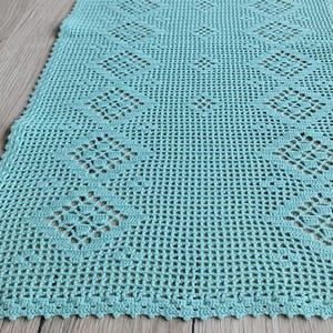 Puede incluir: Un camino de mesa de ganchillo de color turquesa con un patrón de diamantes. El camino de mesa tiene un borde festoneado.