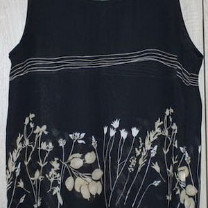 Pode incluir: Uma blusa preta sem mangas com estampa floral branca e finas listras brancas no peito.