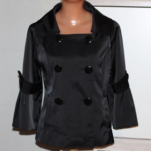 May include: A black satin jacket with a double-breasted closure and four black buttons. The jacket has long sleeves with a bell shape at the cuffs and a square neckline.
