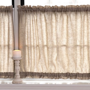 May include: Two beige linen cafe curtains with a gathered ruffle at the top and bottom. A white candle holder with a white candle is in front of the curtains.