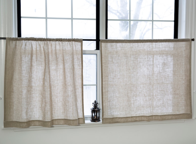Puede incluir: Dos cortinas de caf&eacute; de lino beige cuelgan de una barra de cortina negra frente a una ventana. Una peque&ntilde;a linterna de metal negro se encuentra en el alf&eacute;izar de la ventana.