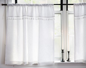 May include: White sheer curtains with a tassel trim hang from a black curtain rod in front of a window. Two black candle holders with white candles are on the window sill.