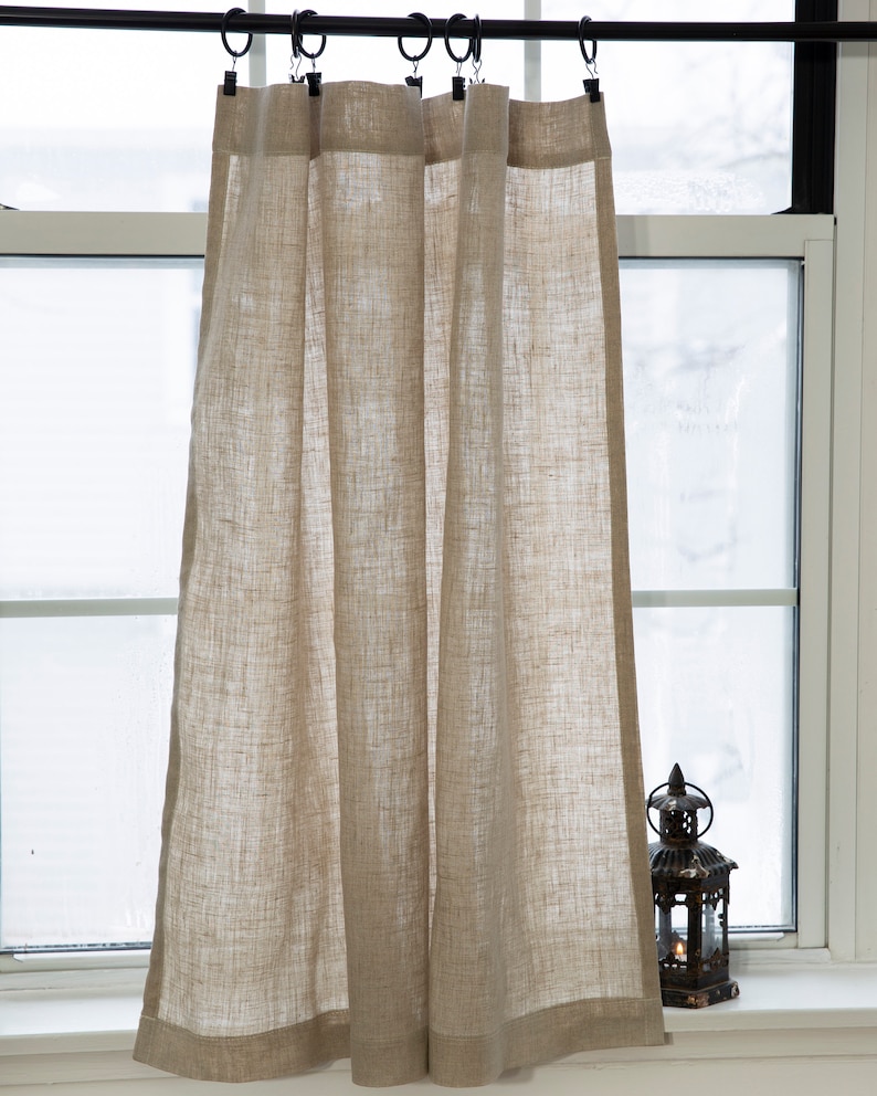 Puede incluir: Un par de cortinas de caf&eacute; de lino natural con una textura sutil cuelgan de una barra de cortina negra. Las cortinas est&aacute;n fruncidas en la parte superior y tienen un dobladillo simple en la parte inferior.