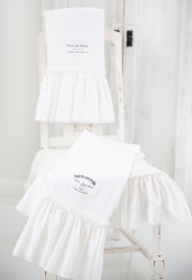 May include: Two white kitchen towels with ruffled edges. The top towel has the text "VILLE DE PARIS" and the bottom towel has the text "HAUTE COUTURE."
