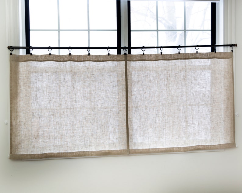 Puede incluir: Un par de cortinas de lino beige colgadas de una barra de cortina negra. Las cortinas son simples y sin adornos, con una textura sutil.