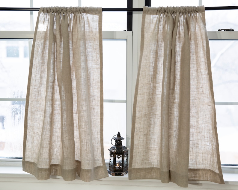 Puede incluir: Dos cortinas de caf&eacute; de lino beige con un ribete superior fruncido y un dobladillo sencillo. Las cortinas est&aacute;n colgadas en una ventana con una barra negra.