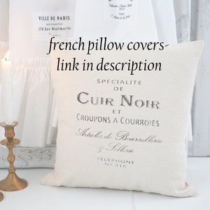 May include: White pillow cover with black text that reads "Specialite de Cuir Noir et Croupons a Courroies Articles de Bourrelterie Sellerie Telephone N&deg; 216".
