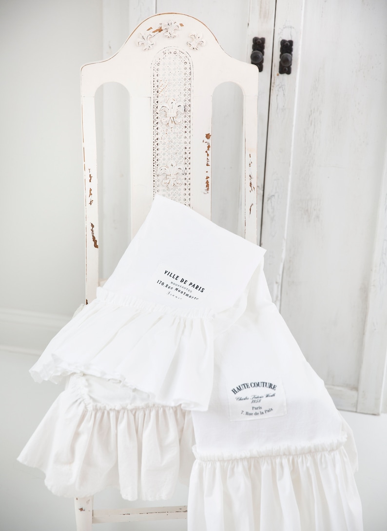 May include: Two white cotton tea towels with ruffled edges. The top towel has the text "Ville de Paris" and "Souvenirs" with the address "170 Rue Montmartre, Paris". The bottom towel has the text "Haute Couture" with the address "Chambre Syndicale de la Haute Couture, Paris, 7 Rue de la Paix".
