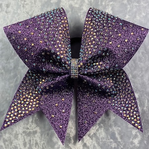 May include: Purple cheer bow with iridescent rhinestones. The bow is made of glitter fabric and has a large, full shape.