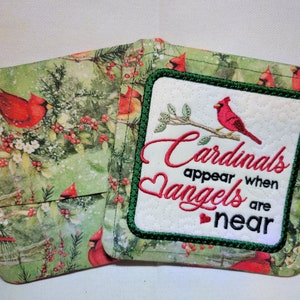 May include: Two green and white fabric coasters with a red cardinal design. One coaster has the text "Cardinals appear when angels are near" embroidered on it.