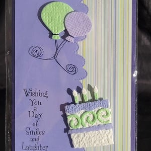 May include: Purple birthday card with a green and purple balloon, a cake with candles, and the text "Wishing You a Day of Smiles and Laughter".