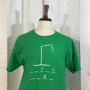 Puede incluir: Camiseta verde con un dibujo blanco de una horca con un signo de interrogación encima. El texto "TRY" y "R" está escrito debajo del dibujo.