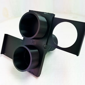 May include: A black 3D-printed object with two cylindrical openings and a circular opening. The object has a rectangular base and appears to be a holder or mount. The design is angular and geometric.