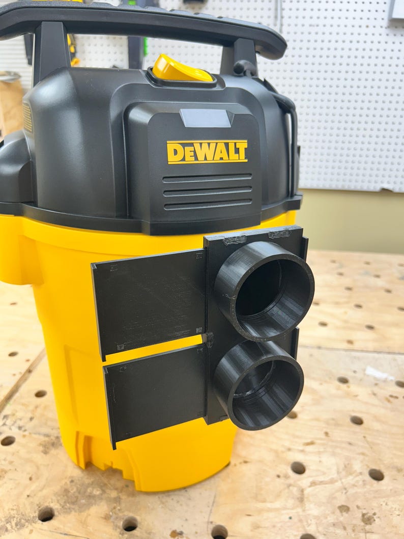 May include: A yellow and black DEWALT wet/dry vacuum with a black attachment featuring two circular openings. The DEWALT logo is prominently displayed in yellow on the front of the vacuum.