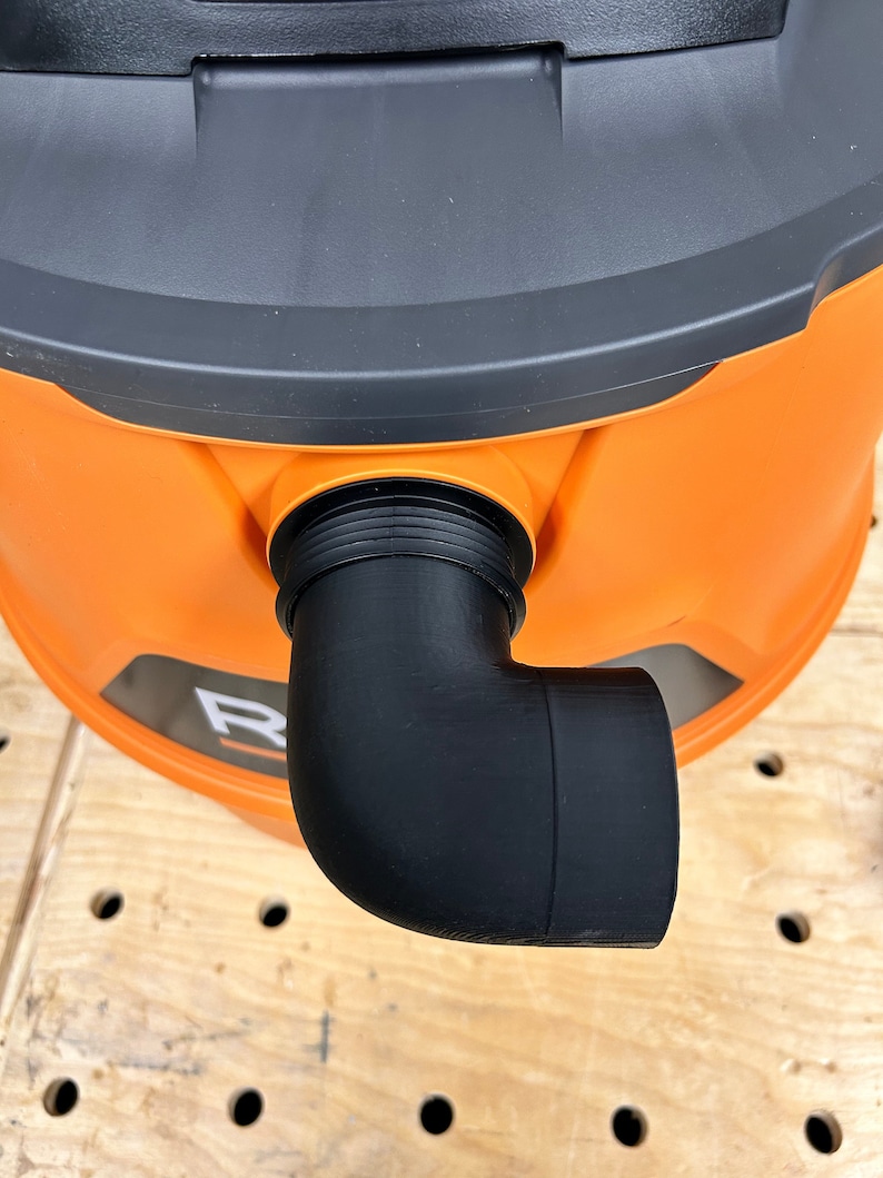 Puede incluir: Primer plano de una conexi&oacute;n de tubo de codo de 90 grados de pl&aacute;stico negro unida a una aspiradora naranja.
