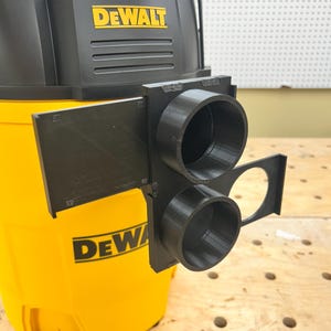 May include: A black 3D-printed adapter attached to a yellow and black DEWALT wet/dry vacuum. The adapter has two circular openings and a rectangular shape. The DEWALT logo is visible on the vacuum.