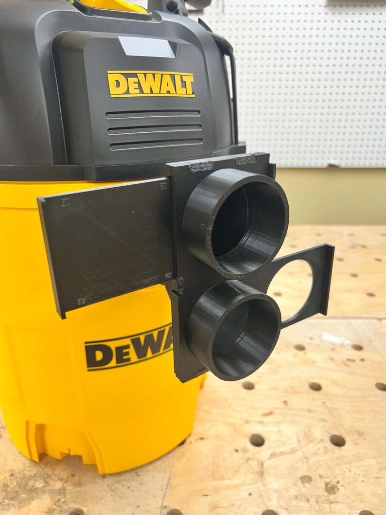 May include: A black 3D-printed adapter attached to a yellow and black DEWALT wet/dry vacuum. The adapter has two circular openings and a rectangular shape. The DEWALT logo is visible on the vacuum.