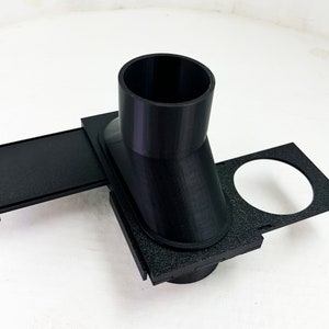 May include: A black 3D-printed object with a cylindrical top and a rectangular base. The base has a sliding tray and a circular cutout. The object is designed for a specific function, likely related to organization or assembly.
