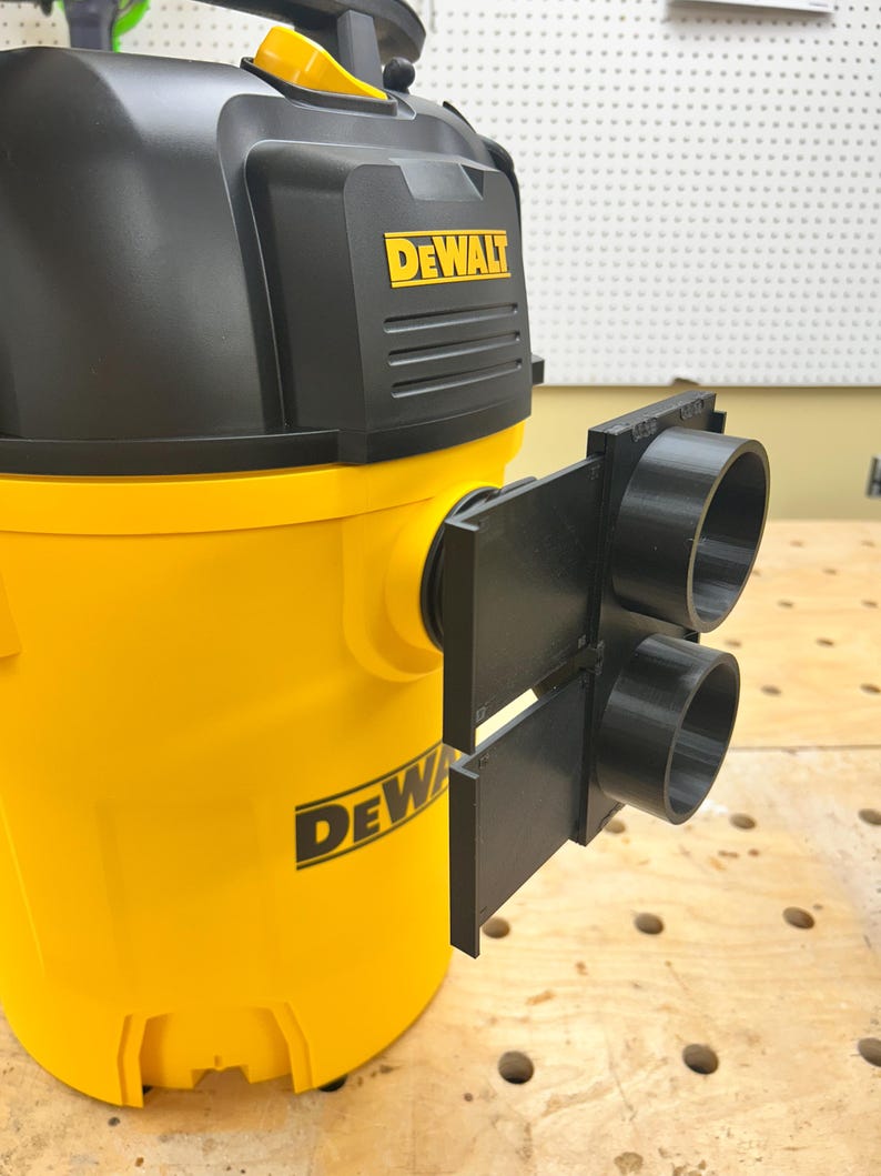 May include: A yellow and black DeWalt wet/dry vacuum with a black attachment. The vacuum has the DeWalt logo in yellow. The attachment has two black circular openings. The vacuum is on a wooden surface.