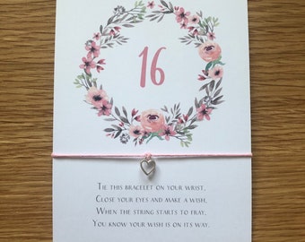 May include: A pink and white floral wreath with the number 16 in the center. The wreath is on a white card with the text "A little birthday wish... Tie this bracelet on your wrist, close your eyes and make a wish, when the string starts to fray, you know your wish is on its way."