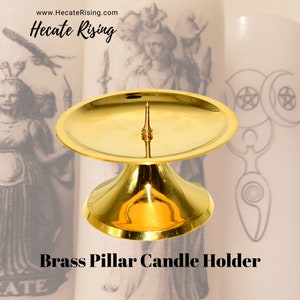 May include: A gold brass pillar candle holder with a round base and a spike on top. The holder is designed to hold a pillar candle.
