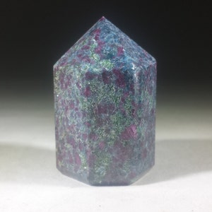 May include: A dark blue and purple gemstone with a faceted, pointed top. The gemstone has a rough, textured surface.
