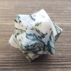May include: A white and green agate star shaped crystal. The crystal has a white base with green swirls and patterns.