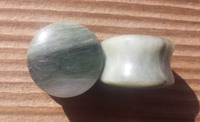 May include: Two green and white stone ear gauges. The larger gauge is a cylinder shape and the smaller gauge is a flat disc.