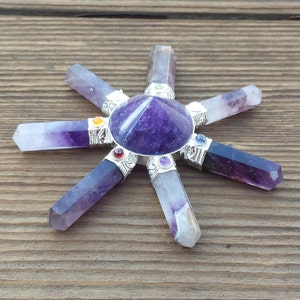 May include: Amethyst crystal grid with seven points, each point is a purple crystal with a silver band and a small colored gemstone. The center of the grid is a purple amethyst pyramid.