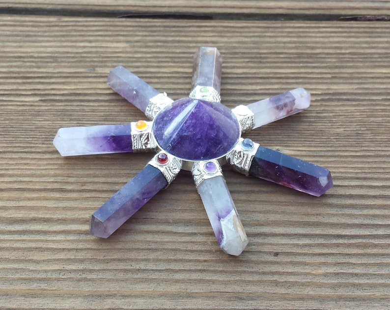 May include: Amethyst crystal grid with seven points, each point is a purple crystal with a silver band and a small colored gemstone. The center of the grid is a purple amethyst pyramid.