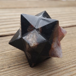 May include: A black and red star-shaped crystal with a smooth, polished surface. The crystal is made of natural stone and has a unique, geometric shape.