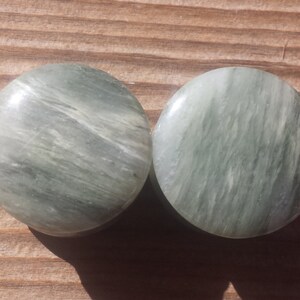 May include: Pair of round green and white stone ear gauges. The gauges have a swirling pattern.