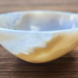 May include: A small, round bowl with a smooth, polished surface. The bowl has a light yellow and white color scheme, with a gradient effect. The bowl is likely made of stone or a similar material.