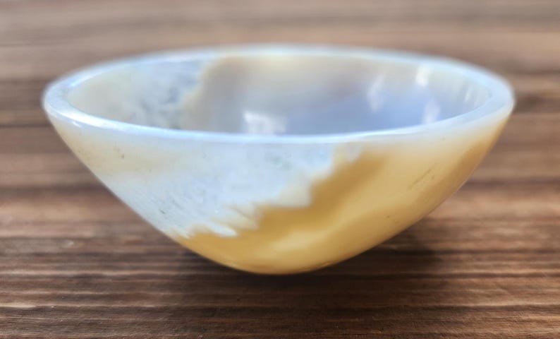 May include: A small, round bowl with a smooth, polished surface. The bowl has a light yellow and white color scheme, with a gradient effect. The bowl is likely made of stone or a similar material.