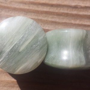May include: Two green and white striped stone ear gauges. The gauges are round and have a smooth, polished finish.