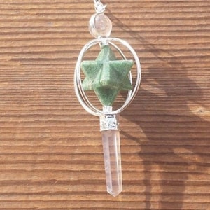 May include: A silver pendulum with a green star-shaped crystal and a clear quartz point. The pendulum is hanging from a silver chain.