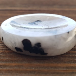 May include: A white and black crystal bowl with a smooth, polished surface. The bowl is made of moonstone and black tourmaline.