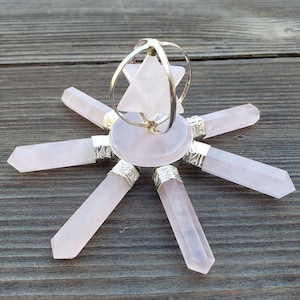 Puede incluir: Una rejilla de cristal de cuarzo rosa con una pirámide de cuarzo rosa giratoria en el centro. La rejilla tiene seis puntos y está hecha de cristales de cuarzo rosa pulidos.